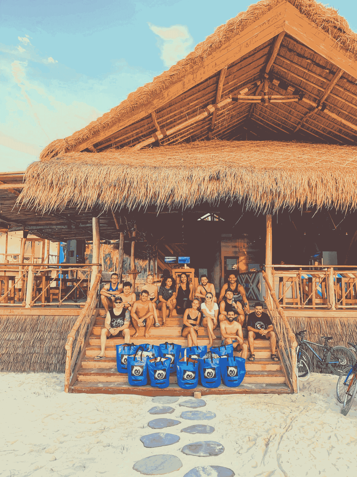 A group gathered on the steps of a thatched beachfront Mad Monkey hostel