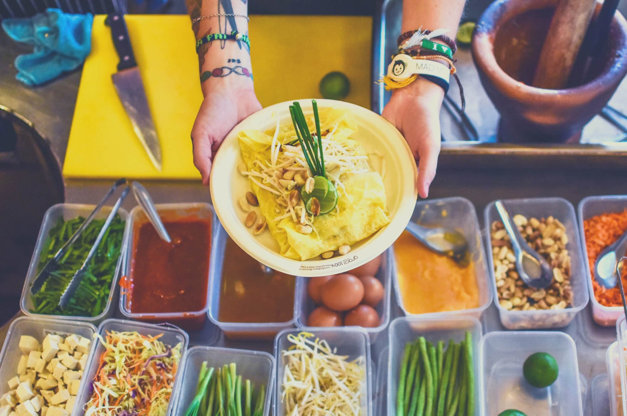 A bowl of noodles being served over trays of fresh local ingredients
