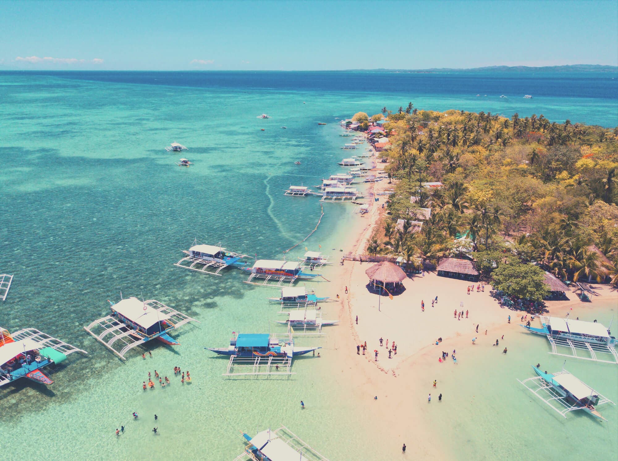 An island beach from the air, outrigger boats moored along the shoreline